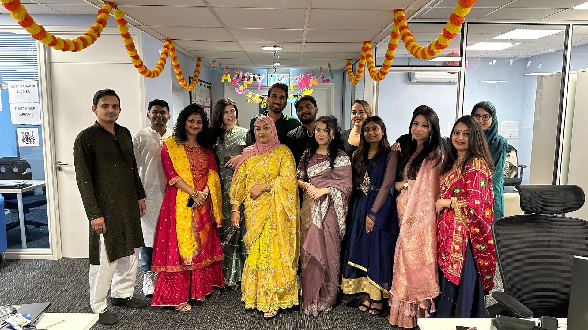 A group of WIC staff and students in colourful sarees and kurtas beneath a 'Happy Diwali' sign