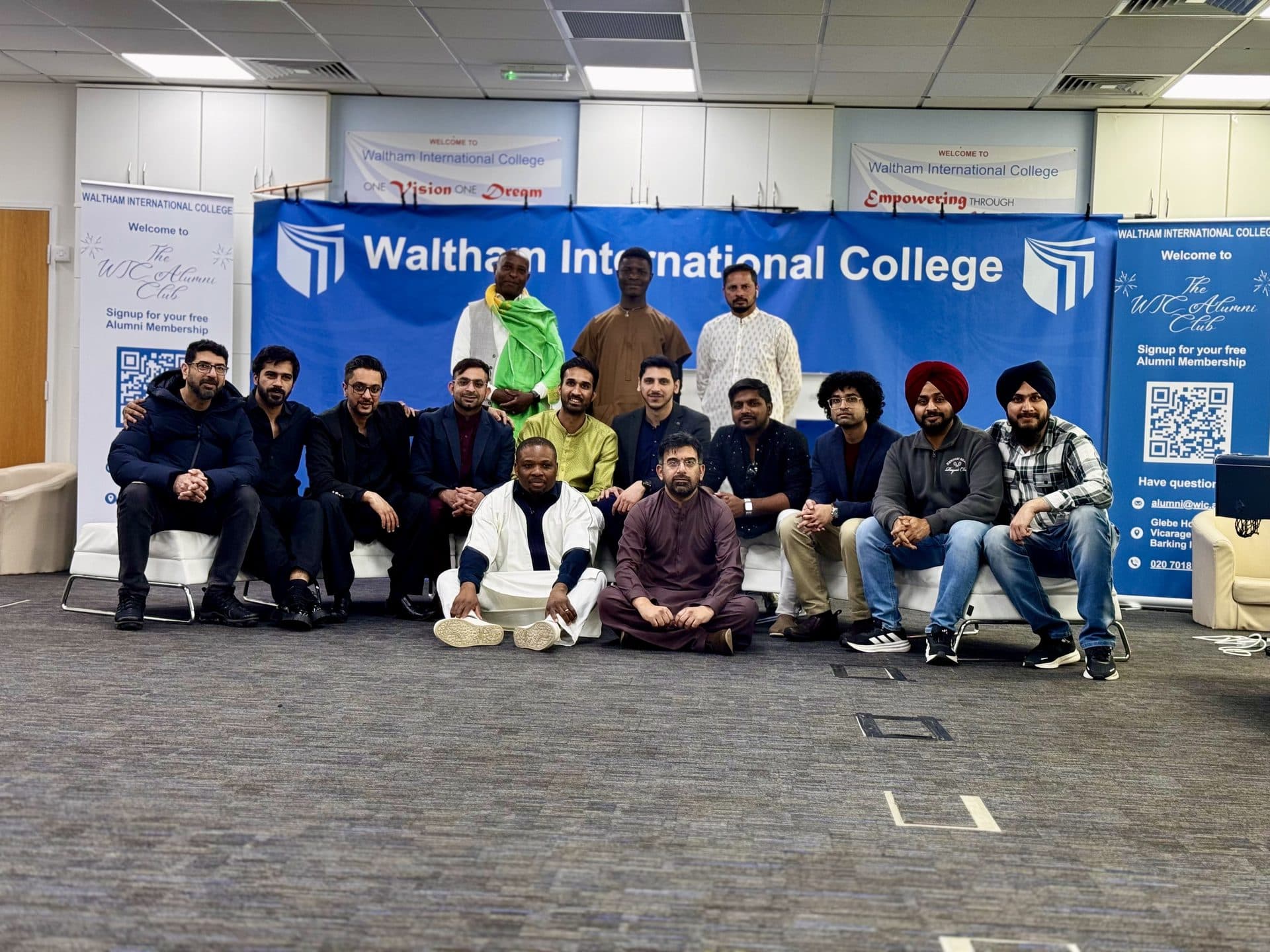 Students and staff in formal and traditional dress posing in front of the Waltham International College banner, London campus
