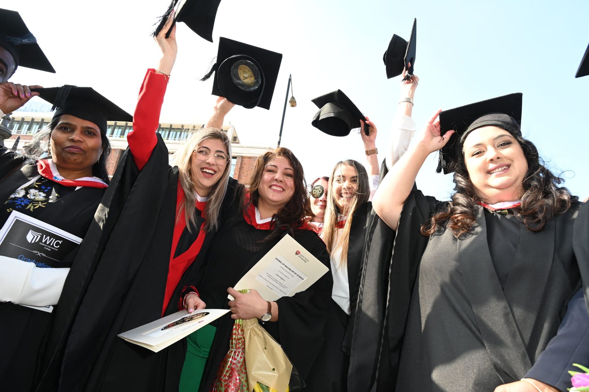 Graduates outdoors in cap and gown throwing their mortarboards in celebration, Class of 2024