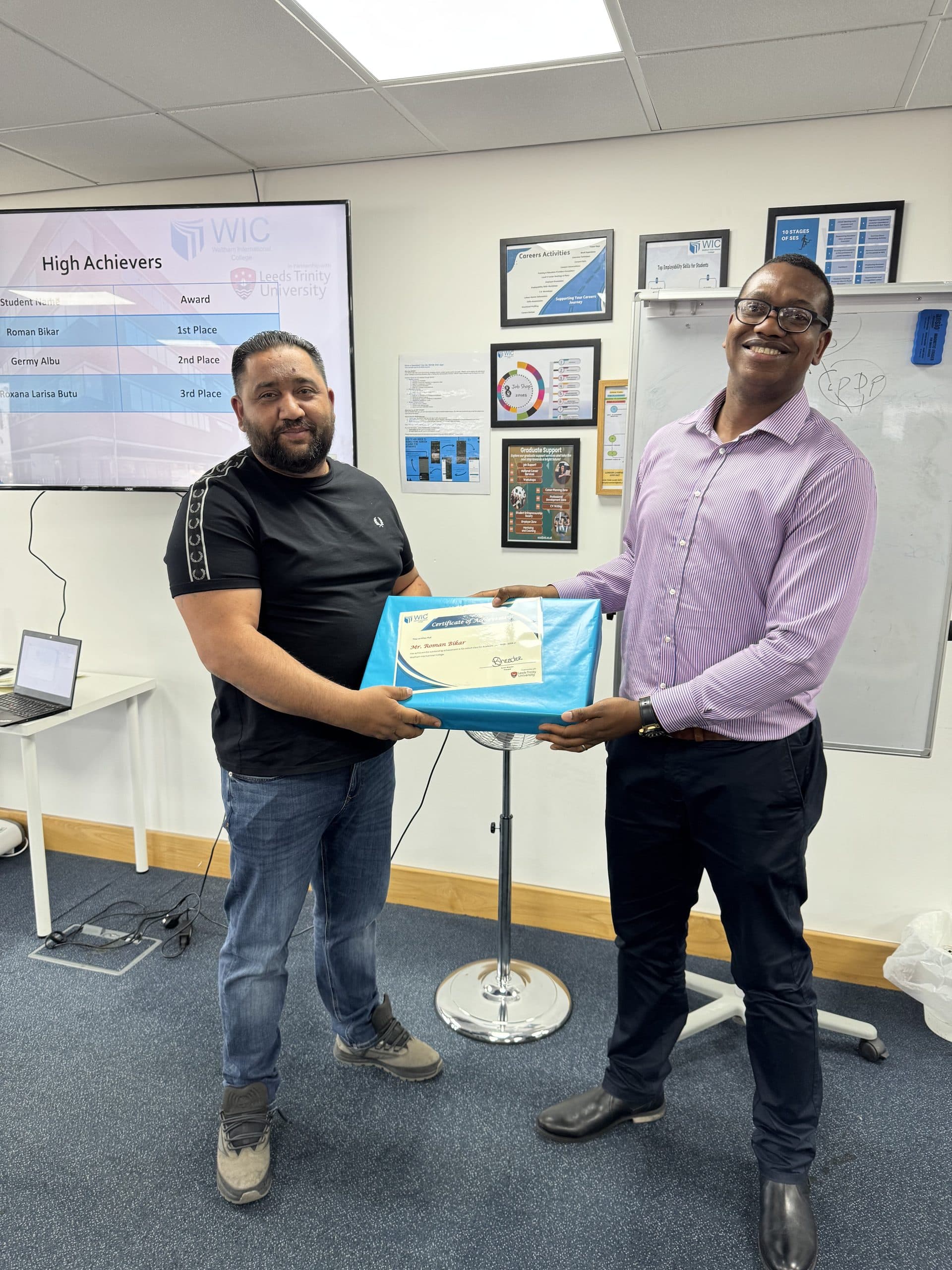Two men shaking hands over a wrapped award, with a High Achievers leaderboard screen behind them