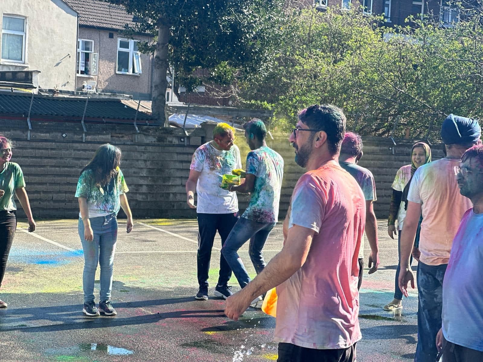 Students at WIC's Holi celebration covered in pink, green, blue and yellow Holi powder, laughing together outdoors