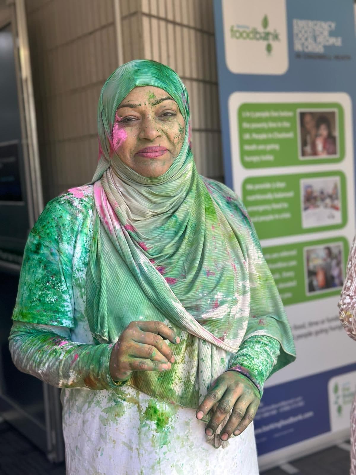 A student in a hijab, her face and clothing covered in green and pink Holi powder