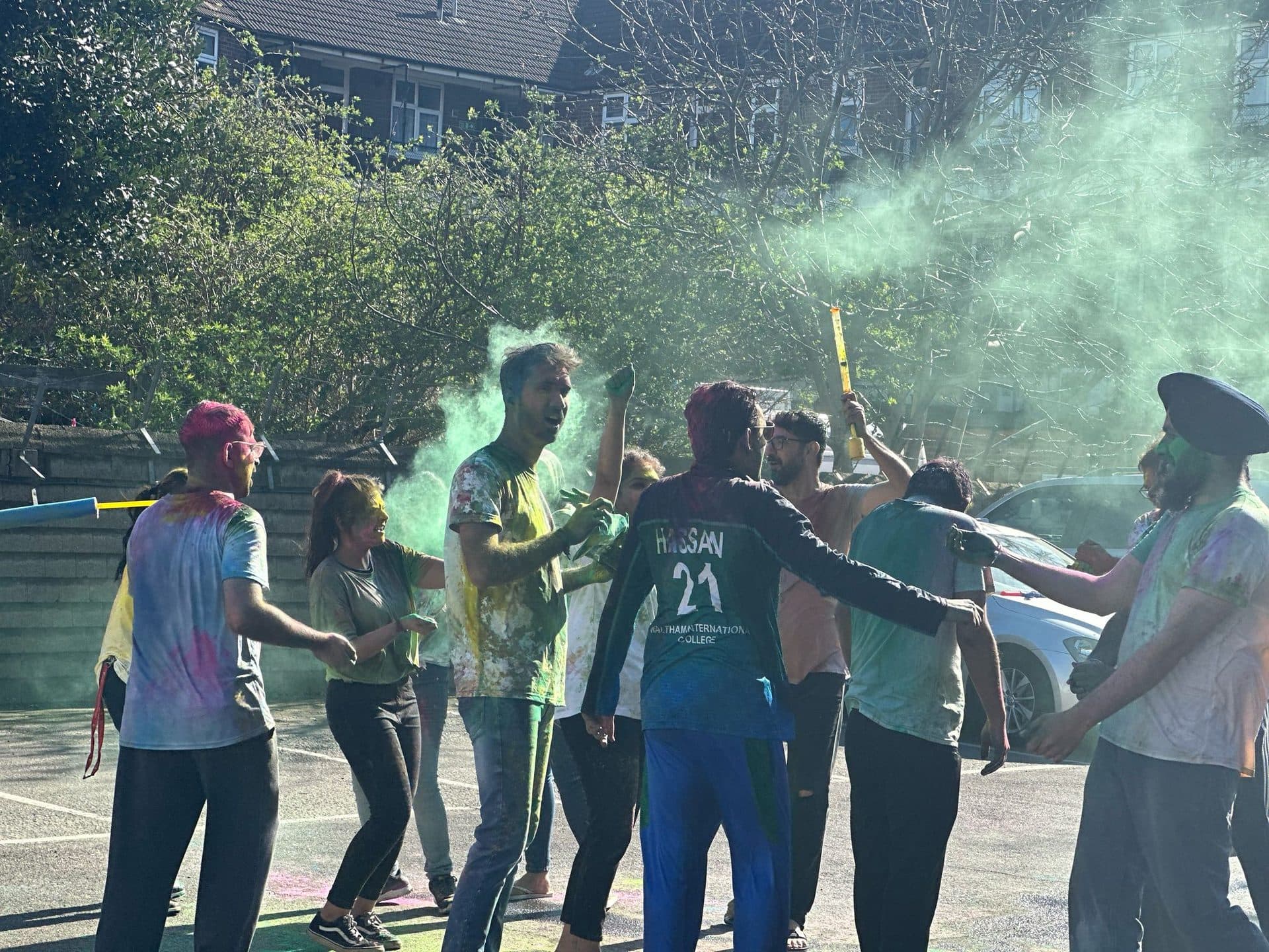 A group of students and staff outdoors covered in colourful Holi powder