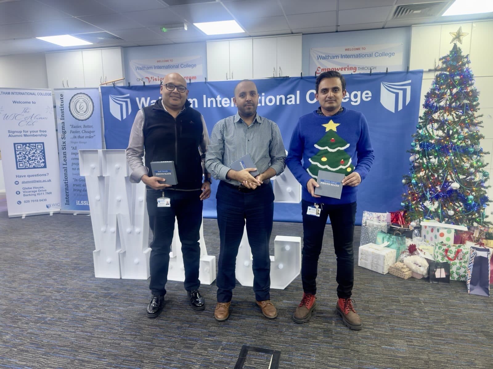 Three WIC staff members holding branded gift boxes in front of the Waltham International College banner